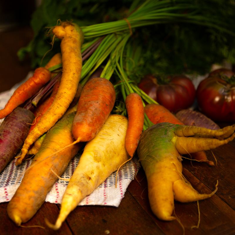 A bunch of heritage carrots with tomatoes on a wooden table