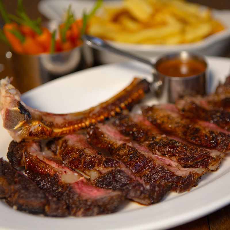 Sliced steak on the bone served with chips and sauce